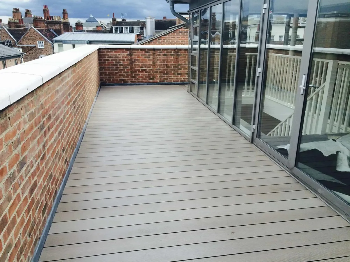 Finished grey roof terrace decking beside a brick parapet and glazed wall
